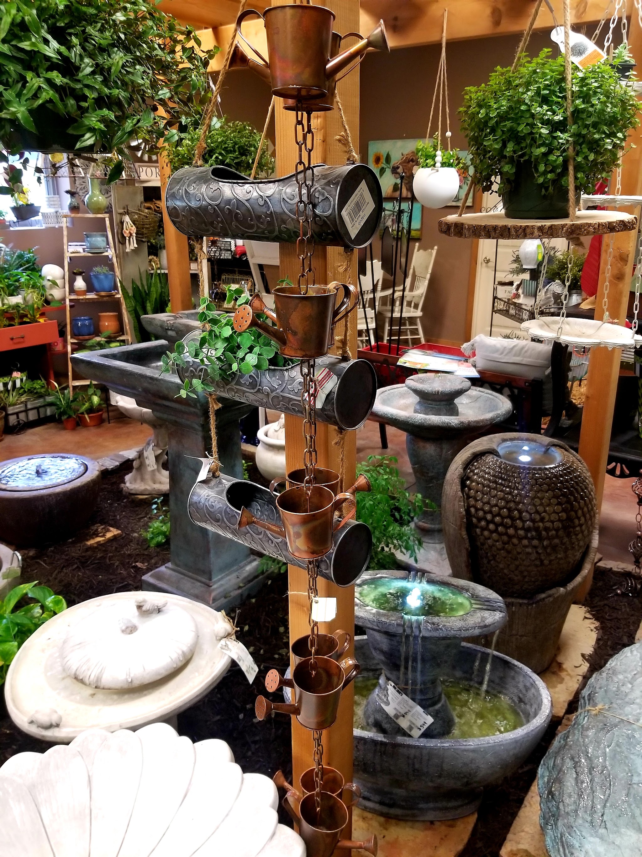 Inside the greenhouse: hanging baskets, a watering can rain chain, birdbaths and running fountains